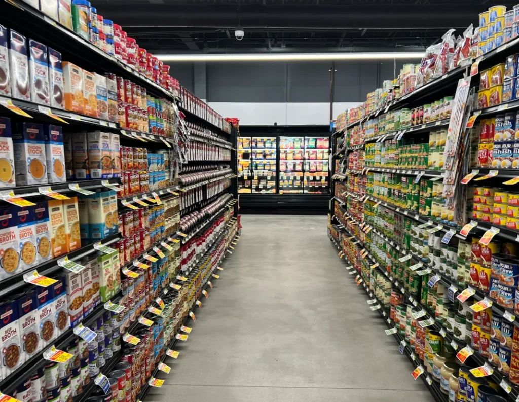 An interior view of a well-stocked grocery store in Hebbal, Mysore, showing long aisles of various products, with refrigerators visible at the far end. The image could be used by Aspire Digital Solutions to highlight their expertise in digital marketing services for retail businesses and supermarkets.