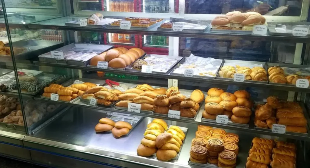 A display case in a home bakery in Whitefield, Bangalore, is filled with rows of pastries, croissants, bread rolls, and baked goods, showcasing the variety of products available. This photo could be used by Aspire Digital Solutions to create promotional content for the bakery.