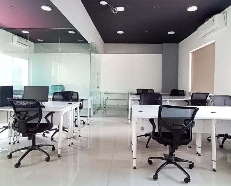 A digitally rendered interior of a clean and modern co-working space in Koramangala, Bangalore, featuring rows of white desks with black ergonomic chairs, and a glass partition separating the main area from another workspace, an image possibly created or managed by Aspire Digital Solutions.