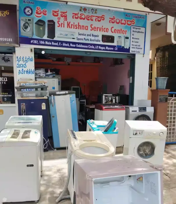 Sri Krishna Service Center in Rajajinagar, a home appliance repair service, with a blue and white sign and various refrigerators, washing machines, and water coolers visible in the foreground, an image that could be used for a promotional campaign by Aspire Digital Solutions.