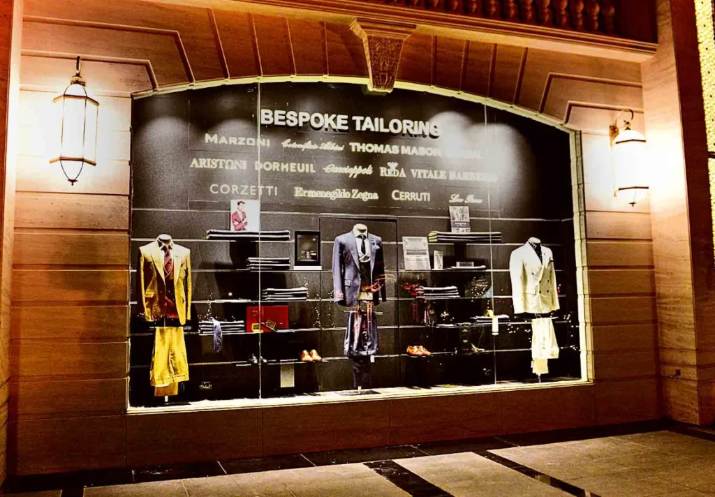 The window of Royal Tailors near NR Mohalla, Mysore, features bespoke tailoring with designer fabric names listed and mannequins showcasing tailored suits. Aspire Digital Solutions can enhance the online presence of such establishments.