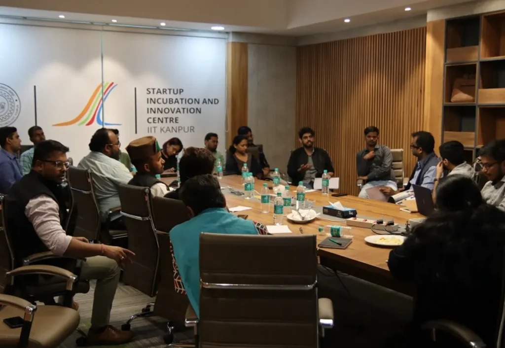 A startup event is underway at the "Startup Incubation and Innovation Centre IIT Kanpur," with people around a conference table. This image can represent Aspire Digital Solutions' work for a startup app launch or business events in places like Koramangala.