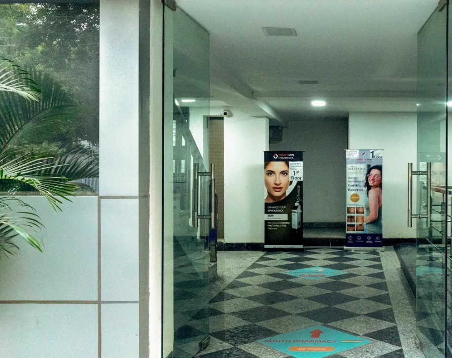A clean, well-lit hallway with large glass panels, a tiled floor, and two vertical banners promoting skincare and beauty products or services. This image is perfect for a company like Aspire Digital Solutions to showcase their marketing work for a skin care clinic or a dermatology center.