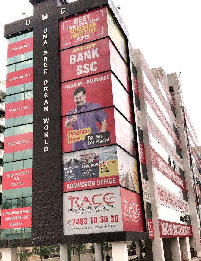 A building in Jayanagar, Bangalore, is covered in banners for the "RACE" competitive exam coaching institute. This image could be used by Aspire Digital Solutions to show their marketing expertise for a coaching center.